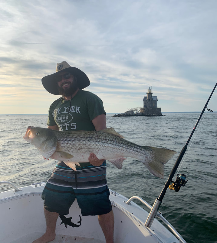 Captain Skippy in front of a Long Island lighthouse holding a trophy striped bass