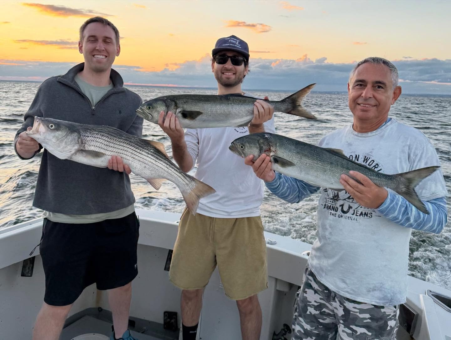 Three anglers holding striped bass and bluefish at sunset
